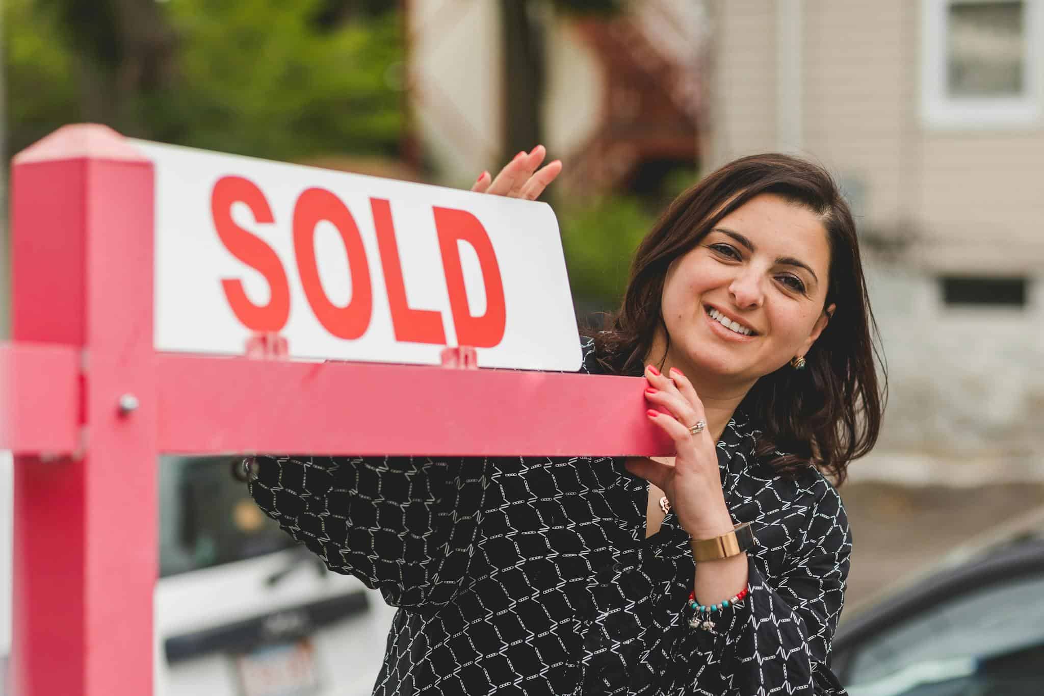 Professional realtor standing next to a Sold sign in front of a residential property.